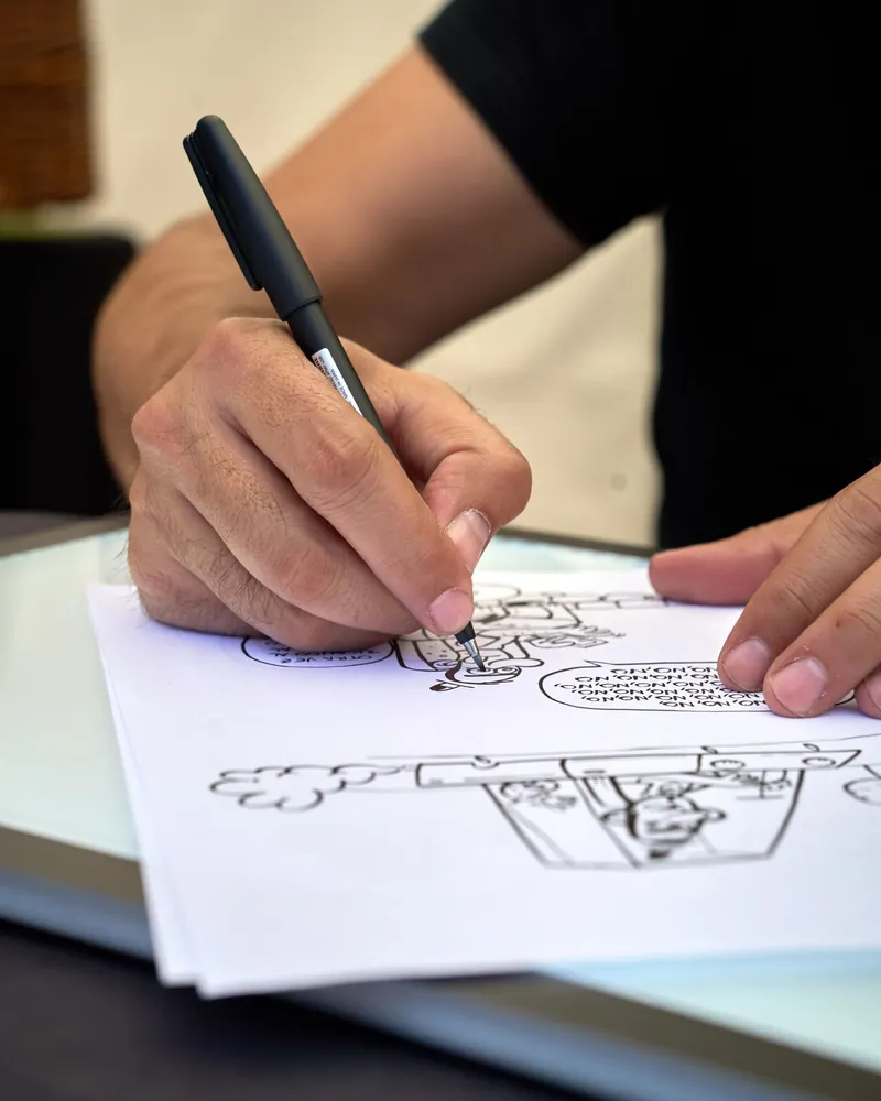 Mano dibujando una figura de trazo caricaturesco sobre papel con rotulador negro